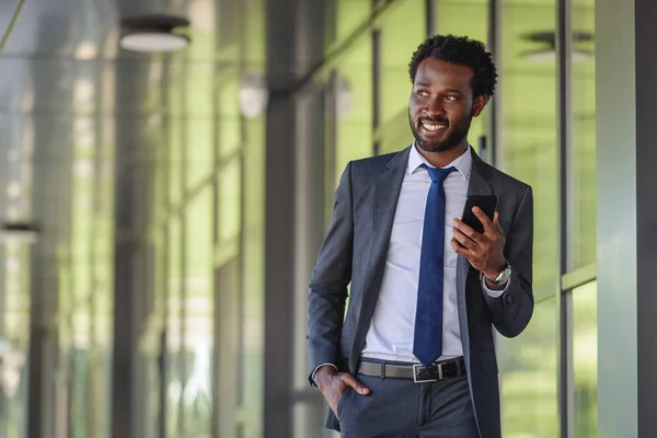 Uśmiechnięty African American Biznesmen Smartphone Spaceru Pobliżu Budynku Biurowego Trzymając — Zdjęcie stockowe