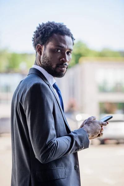Confiante Empresário Afro Americano Olhando Para Câmera Enquanto Usa Smartphone — Fotografia de Stock