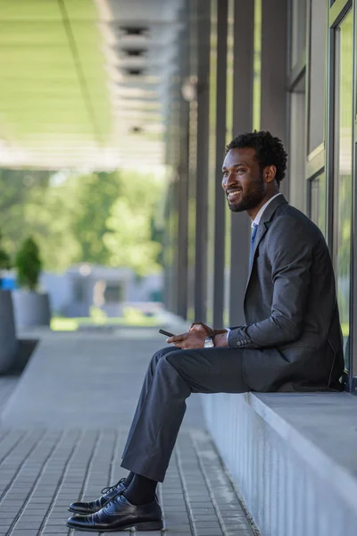Χαρούμενο Αφρικανικό Αμερικανό Επιχειρηματία Που Χρησιμοποιεί Smartphone Και Κοιτάζοντας Μακριά — Φωτογραφία Αρχείου