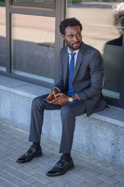 Smiling African American Businessman Looking Away While Sitting Parapet Holding — Stock Photo, Image