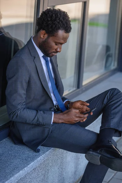 Gutaussehender Afrikanisch Amerikanischer Geschäftsmann Sitzt Auf Brüstung Und Benutzt Smartphone — Stockfoto