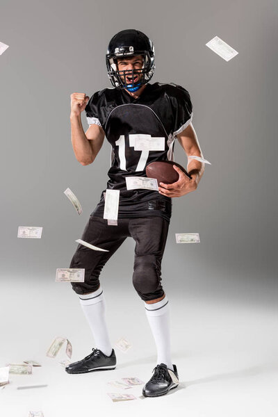 excited American Football player with ball on grey with falling money