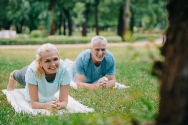 parkta yoga yaparken tahta egzersiz ilerken gülümseyen olgun erkek ve kadının seçici odak