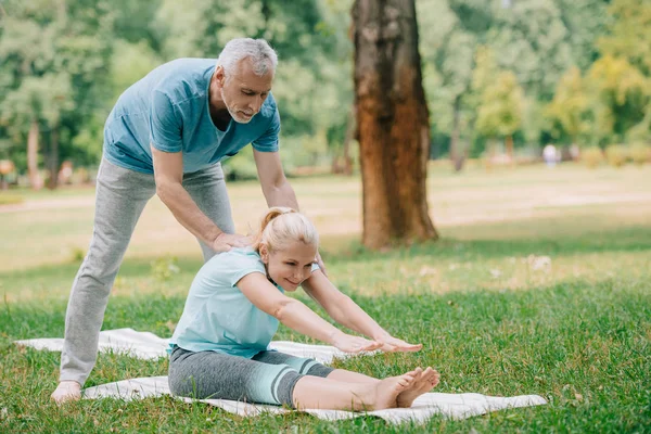 Schöner Reifer Mann Hilft Frau Beim Yoga Auf Rasen Park — Stockfoto