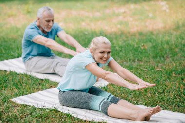 gülümseyen olgun erkek ve kadın yoga yaparken yoga paspaslar üzerinde otururken pozlar