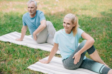 parkta yoga yaparken gülümseyen olgun erkek ve kadın