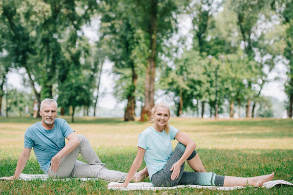 smiling, mature man and woman practicing yoga on green lawn in park
