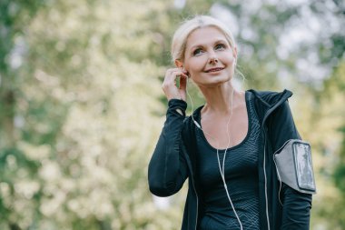gülümseyen olgun sporcu kulaklıkla müzik dinlerken uzağa bakıyor