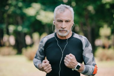 parkta koşarken kulaklıkla müzik dinleyen kendine güvenen olgun sporcu