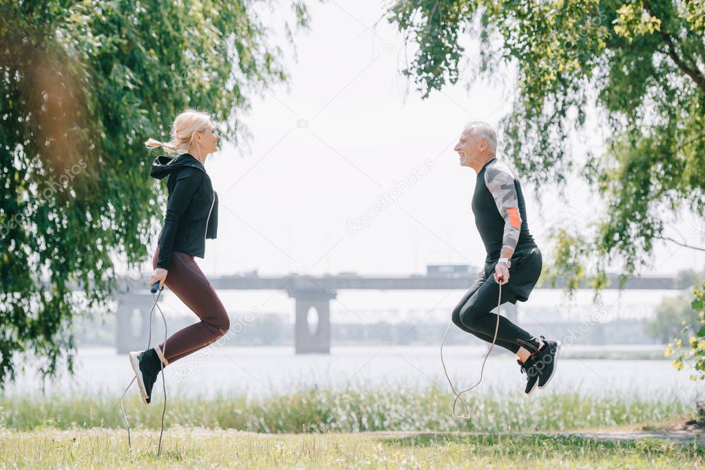 side view of mature sportsman and sportswoman training with jump ropes in park together