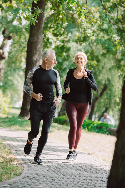 веселый взрослый спортсмен и спортсменка бегают вместе в солнечном парке
