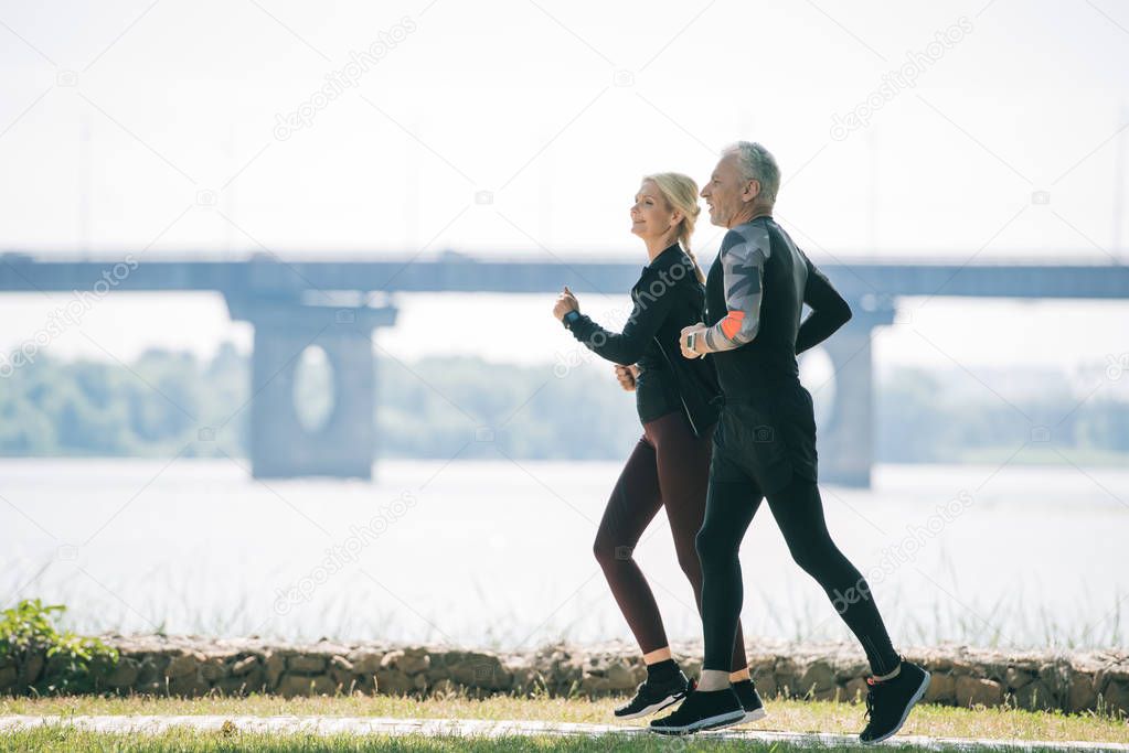 mature sportsman and sportswoman running along riverside in park