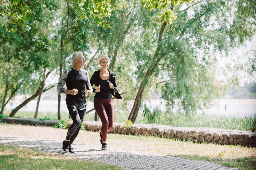 sportive mature sportsman and sportswoman running together in park