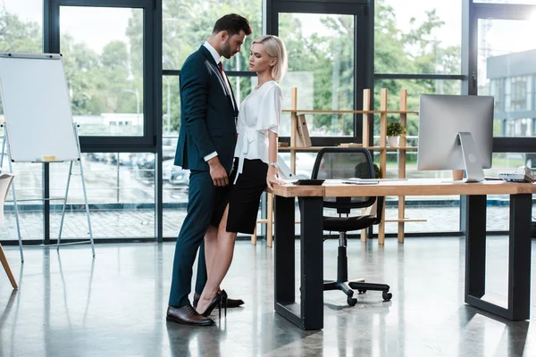 オフィスでいちゃつきながら魅力的な若い女性に触れるハンサムなビジネスマン — ストック写真