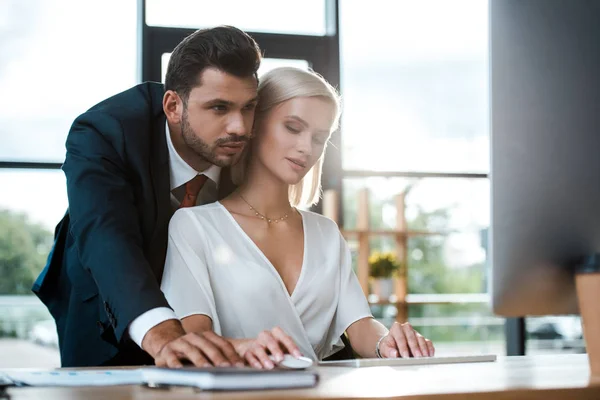 オフィスで魅力的なブロンドの女の子の近くに立ってスーツでひげを生やしたビジネスマンの選択的な焦点 — ストック写真