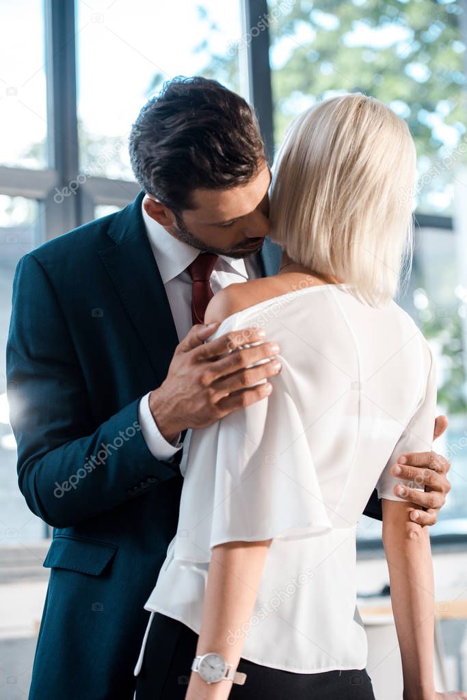 handsome businessman touching blonde woman while flirting in office 