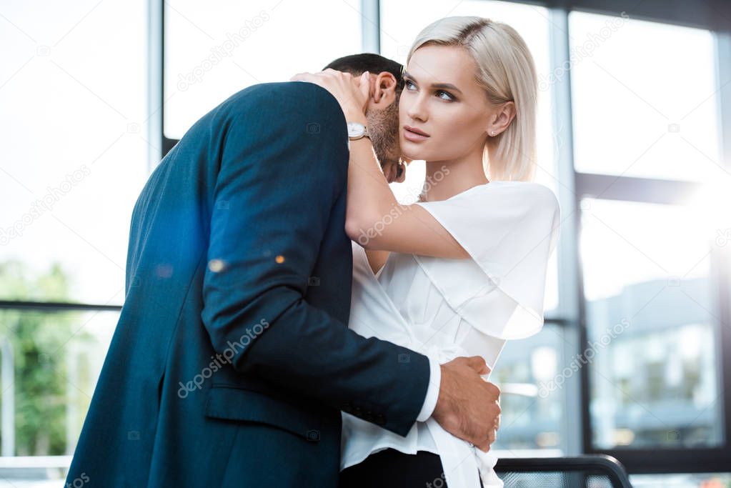 attractive blonde woman hugging with businessman in office 