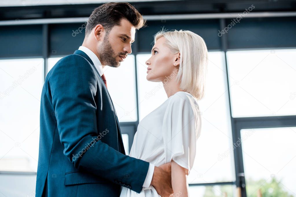 low angle view of bearded man looking at blonde girl while flirting in office 