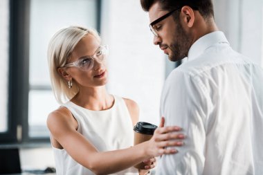 çekici kadın tutan kağıt fincan ve dokunaklı üzgün iş arkadaşı içinde ofis 