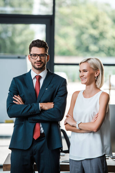 cheerful businessman in glasses and attractive businesswoman standing with crossed arms 