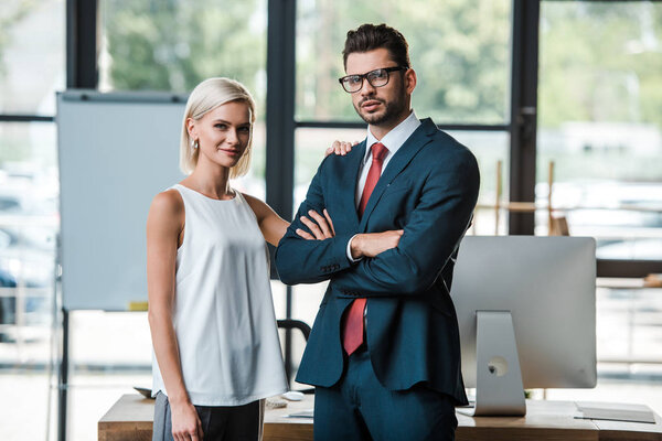 cheerful woman standing near handsome businessman with crossed arms 