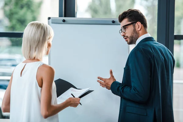 Mujer Rubia Sosteniendo Carpeta Cerca Hombre Negocios Gafas Gestos Oficina — Foto de Stock