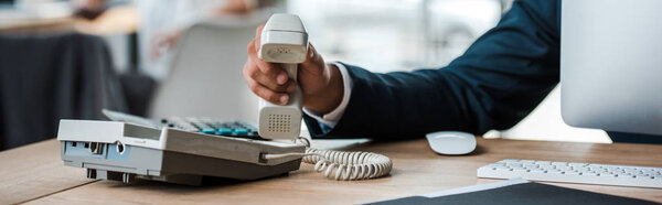panoramic shot of businessman holding retro phone in office 