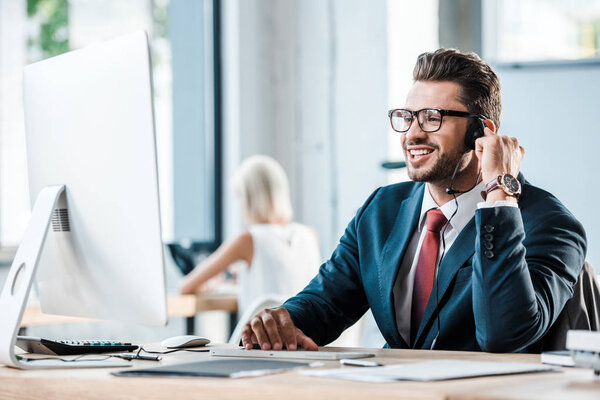 selective focus of happy businessman in headset smiling in office 