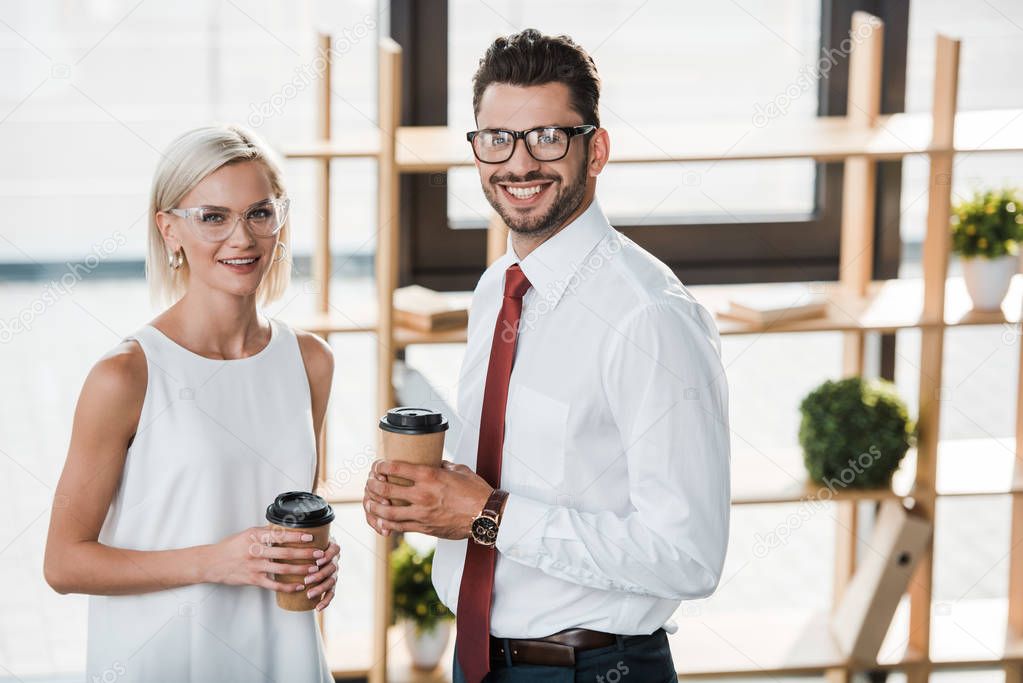 cheerful businessman and businesswoman smiling while holding paper cups 