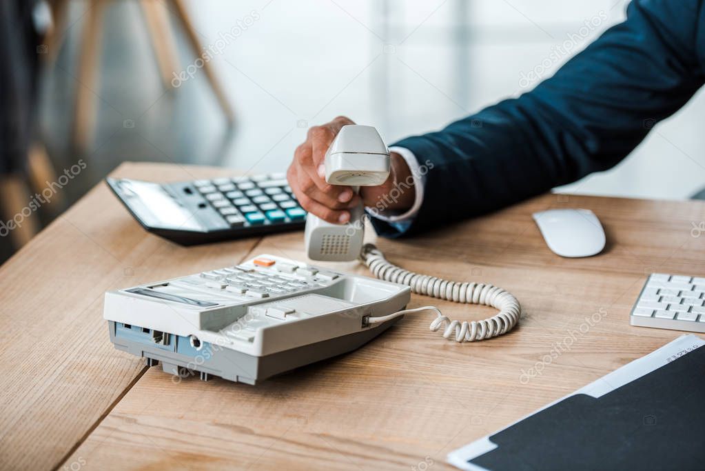 cropped view of businessman holding retro telephone in office 