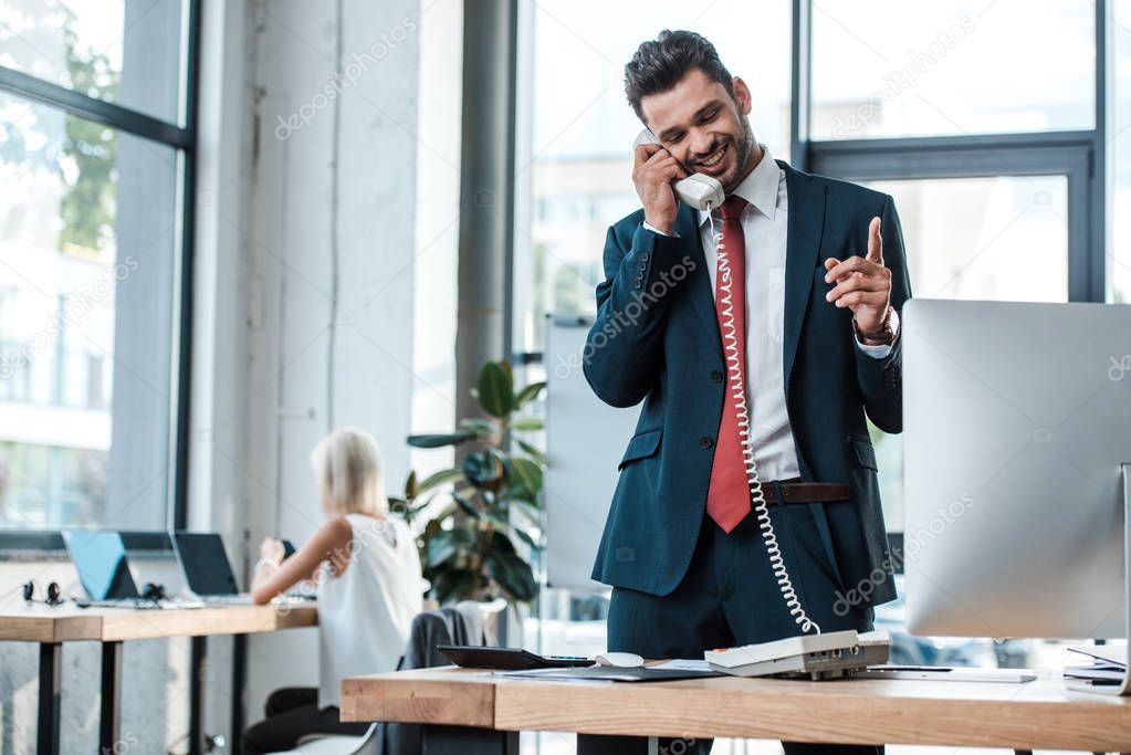 selective focus of happy bearded man talking on retro phone and gesturing in office 