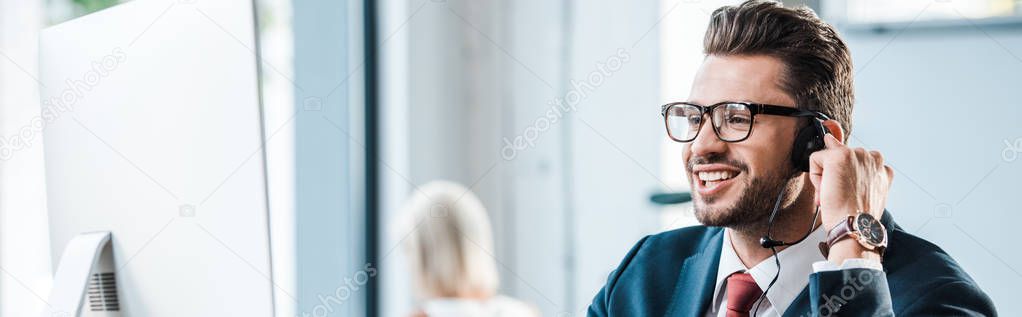 panoramic shot handsome businessman in headset and glasses smiling in office 