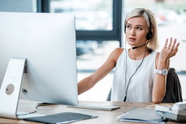 bilgisayar monitörü yakınında ofiste çalışan kulaklıkta güzel sarışın kadın seçici odak 