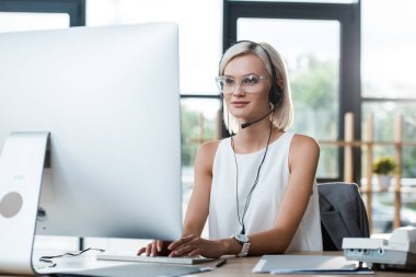 selective focus of happy blonde operator in glasses working in call center  clipart