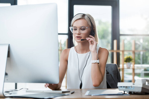 selective focus of attractive blonde operator in glasses working in call center 