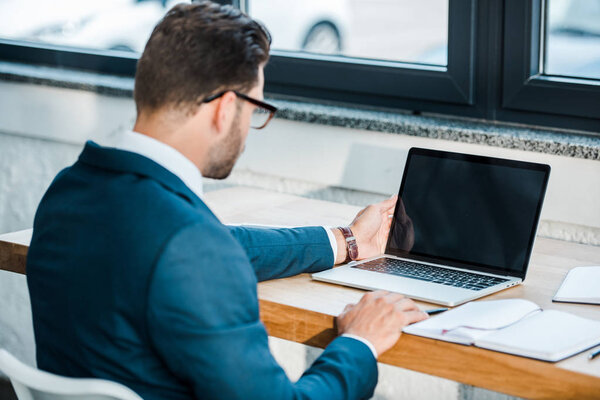 selective focus of laptop with blank screen near businessman in office 