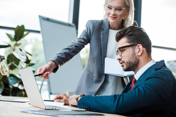 selective focus of man near blonde coworker holding pen near laptop 