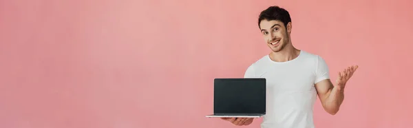 微笑的年轻人在白色T恤的全景镜头显示笔记本电脑与空白屏幕隔离在粉红色 — 图库照片