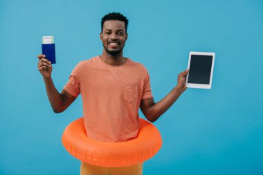 mavi izole boş ekran ile pasaport ve dijital tablet tutan neşeli afrikalı amerikalı adam 