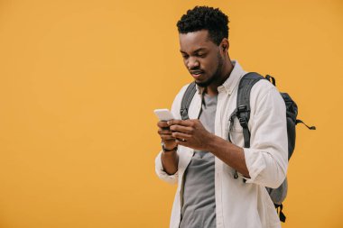 turuncu izole akıllı telefon kullanarak sırt çantası ile yakışıklı afro-amerikan adam