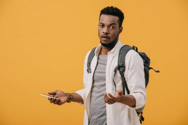 sırt çantası akıllı telefon tutan ve turuncu izole gesturing ile Afrikalı-Amerikalı adam