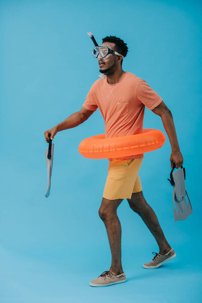 Африканский американец в водолазной маске держит ласты и ходит по синей
 