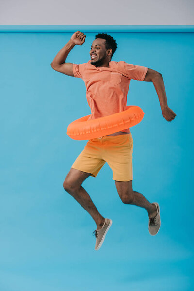 счастливый бородатый африканский американец прыгает с плавательным кольцом на голубом
 