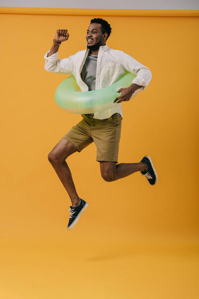Веселый бородатый африканский американец прыгает с плавательным кольцом на оранжевом
