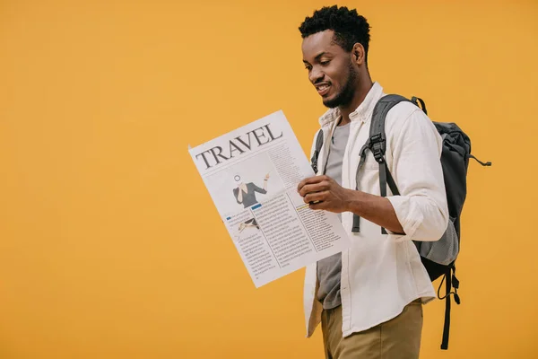 陽気なアフリカ系アメリカ人男性がバックパックを持って立ち オレンジ色に孤立した旅行新聞を読む — ストック写真