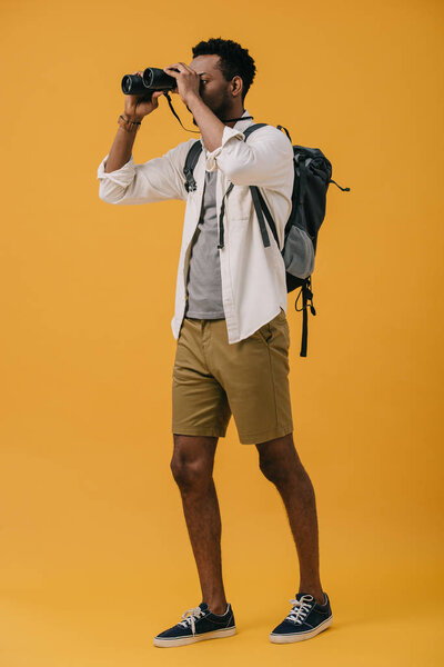 african american man looking through binoculars on orange 
