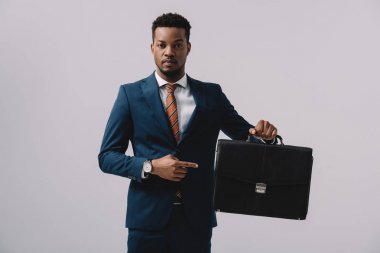 african american man pointing with finger at briefcase isolated on grey  clipart