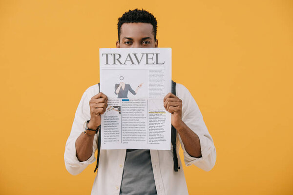 curly african american man covering face with travel newspaper isolated on orange