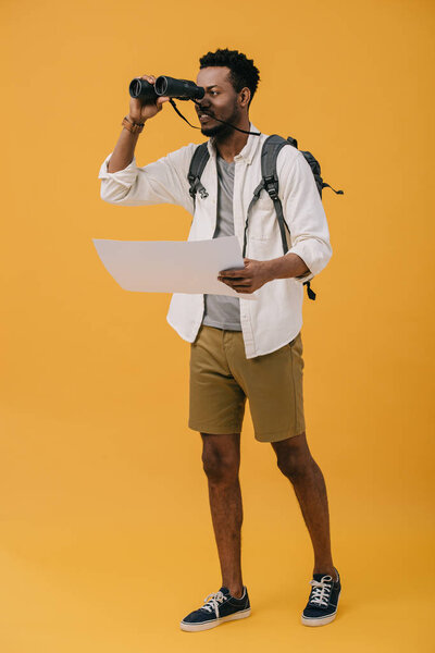 handsome african american man holding blank paper and looking through binoculars  on orange 
