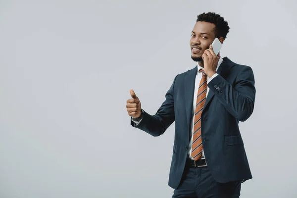 幸せなアフリカ系アメリカ人のビジネスマンは親指を上げて 灰色で隔離されたスマートフォンで話す — ストック写真